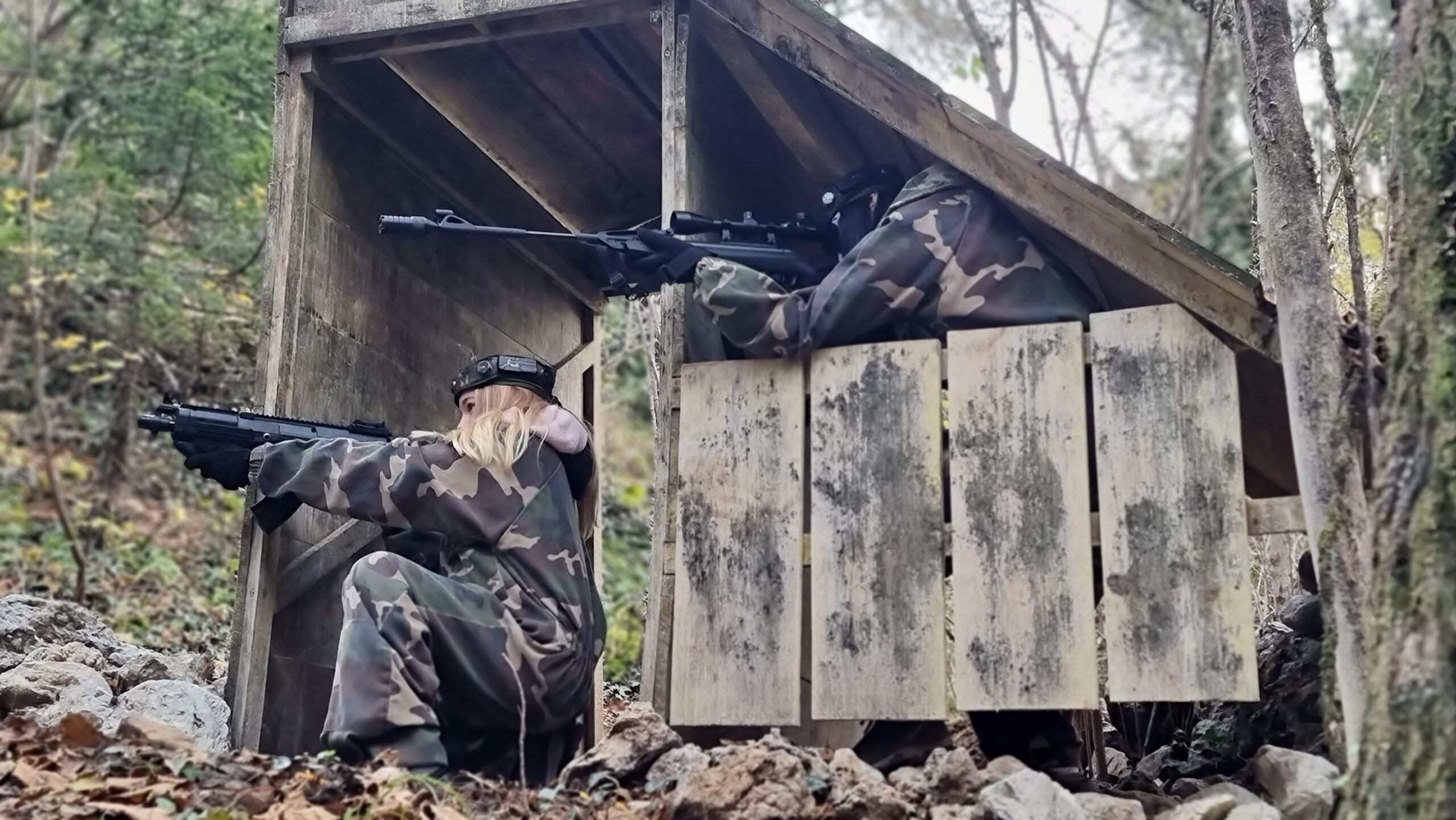 Due giocatori di laser tag si riparano dietro una struttura in legno nel bosco